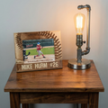 Wooden picture frame with a baseball player photo and name / number engraved text, next to a lamp on a wooden table.