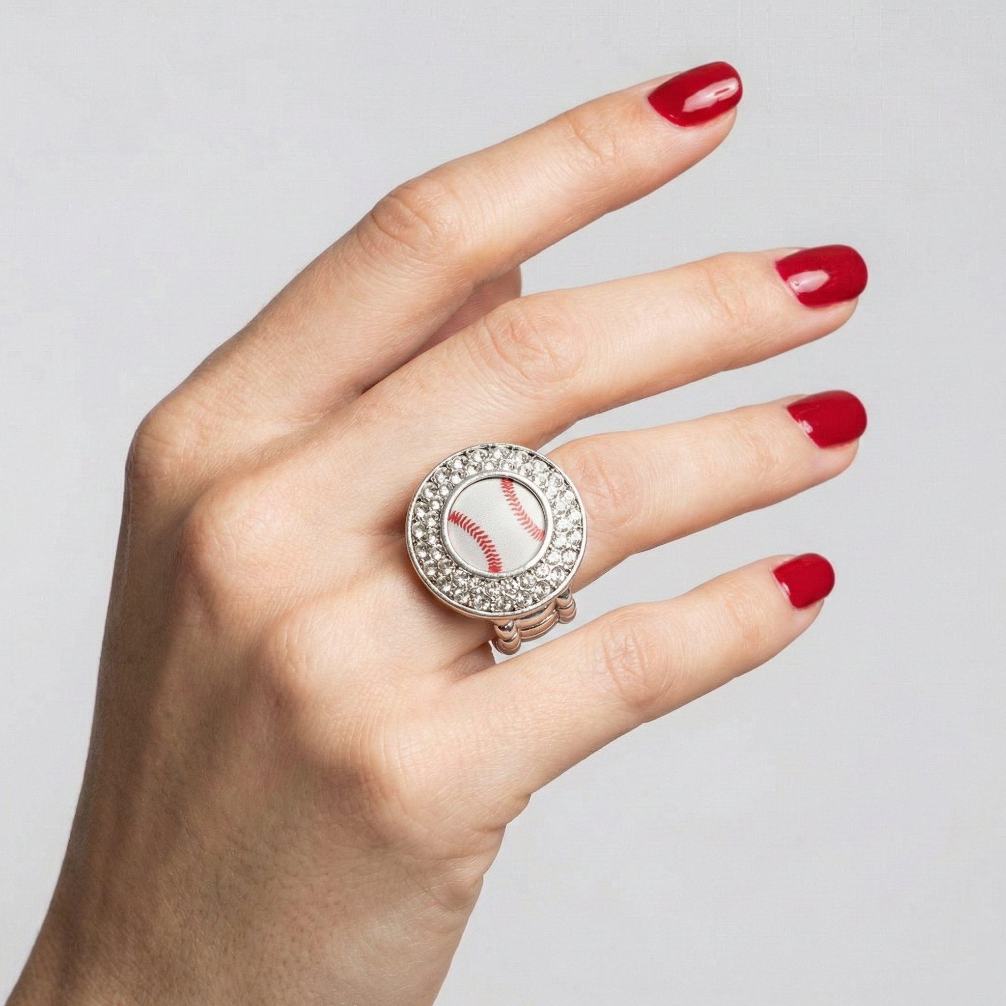 Hand wearing a ring with a baseball design on a plain background