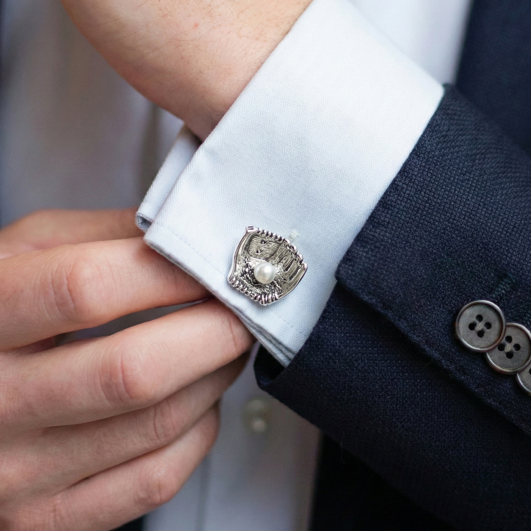 Close-up of a person wearing a baseball glove cufflink on a suit sleeve.