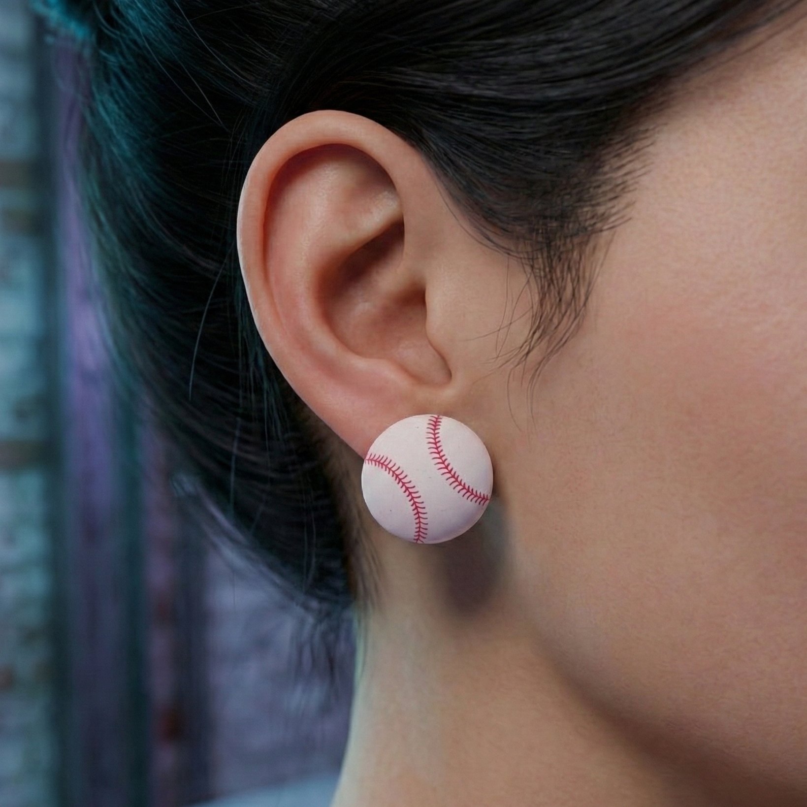 Close-up of an ear wearing a baseball-shaped earring with a blurred background