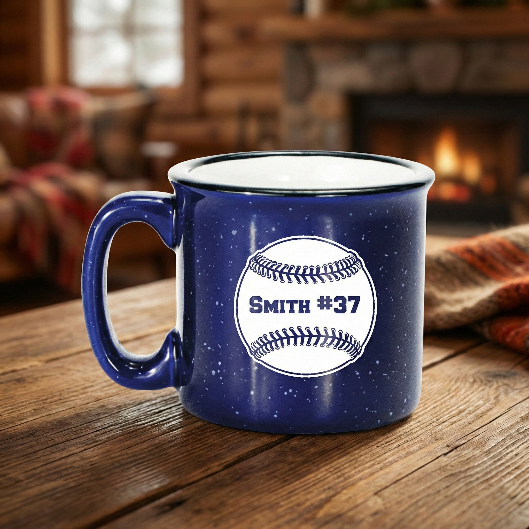 Blue campfire mug with a baseball-themed design on a wooden table in a cozy room with a fireplace.