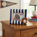 Baseball theme picture frame with a baby photo on a wooden surface, with a baseball and lamp in the background.