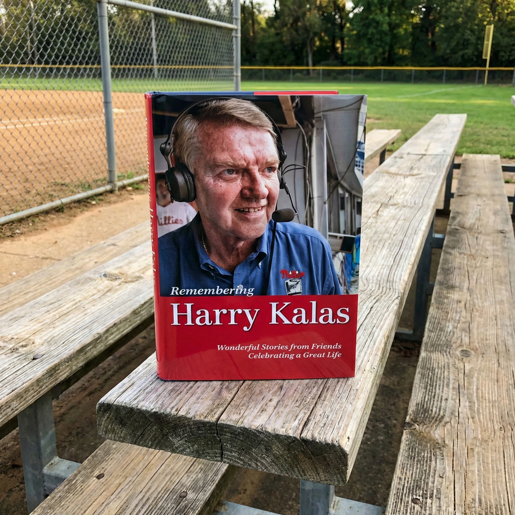 Book titled 'Remembering Harry Kalas' on a wooden bench with a baseball field background