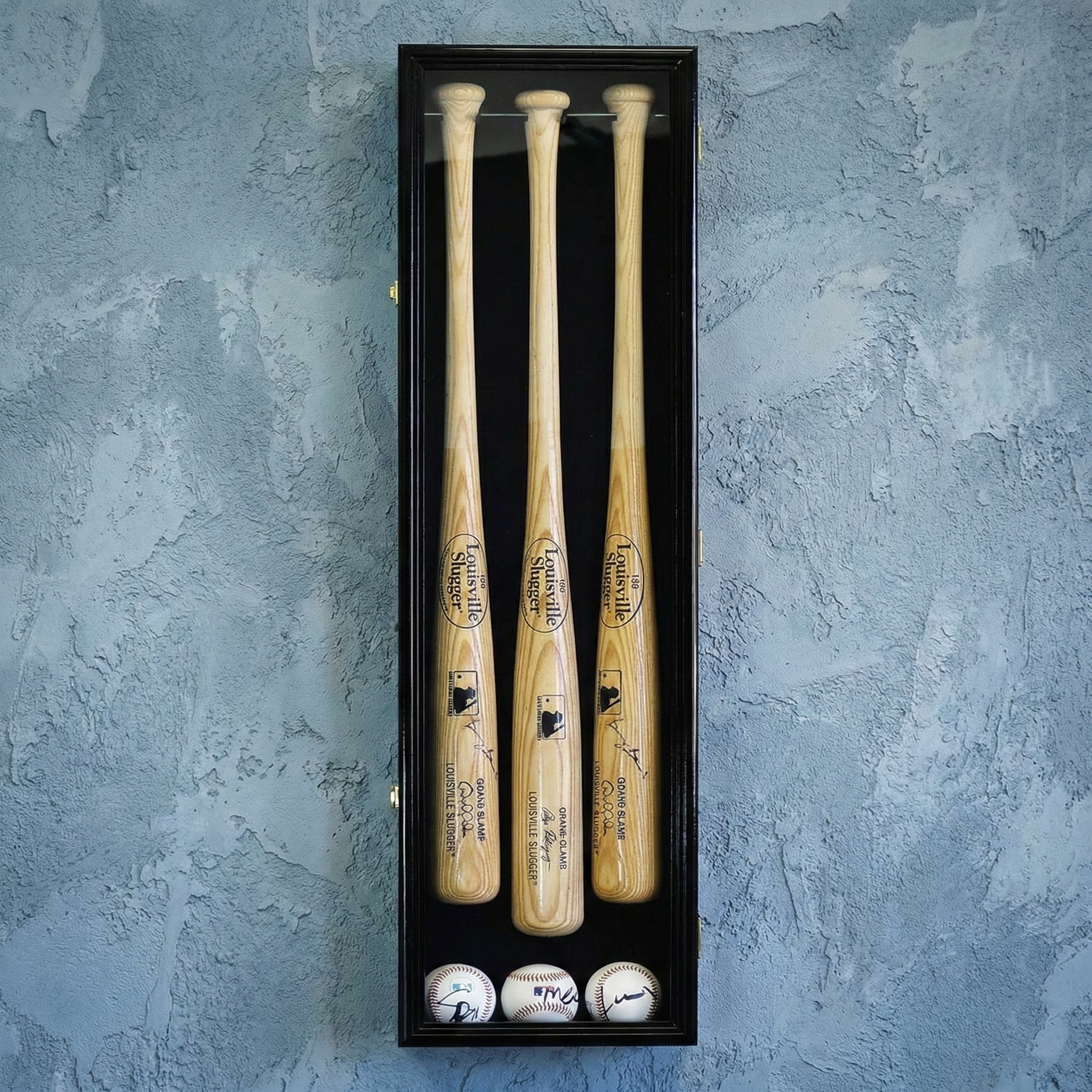 Three wooden baseball bats in a black display case with baseballs on a textured blue background