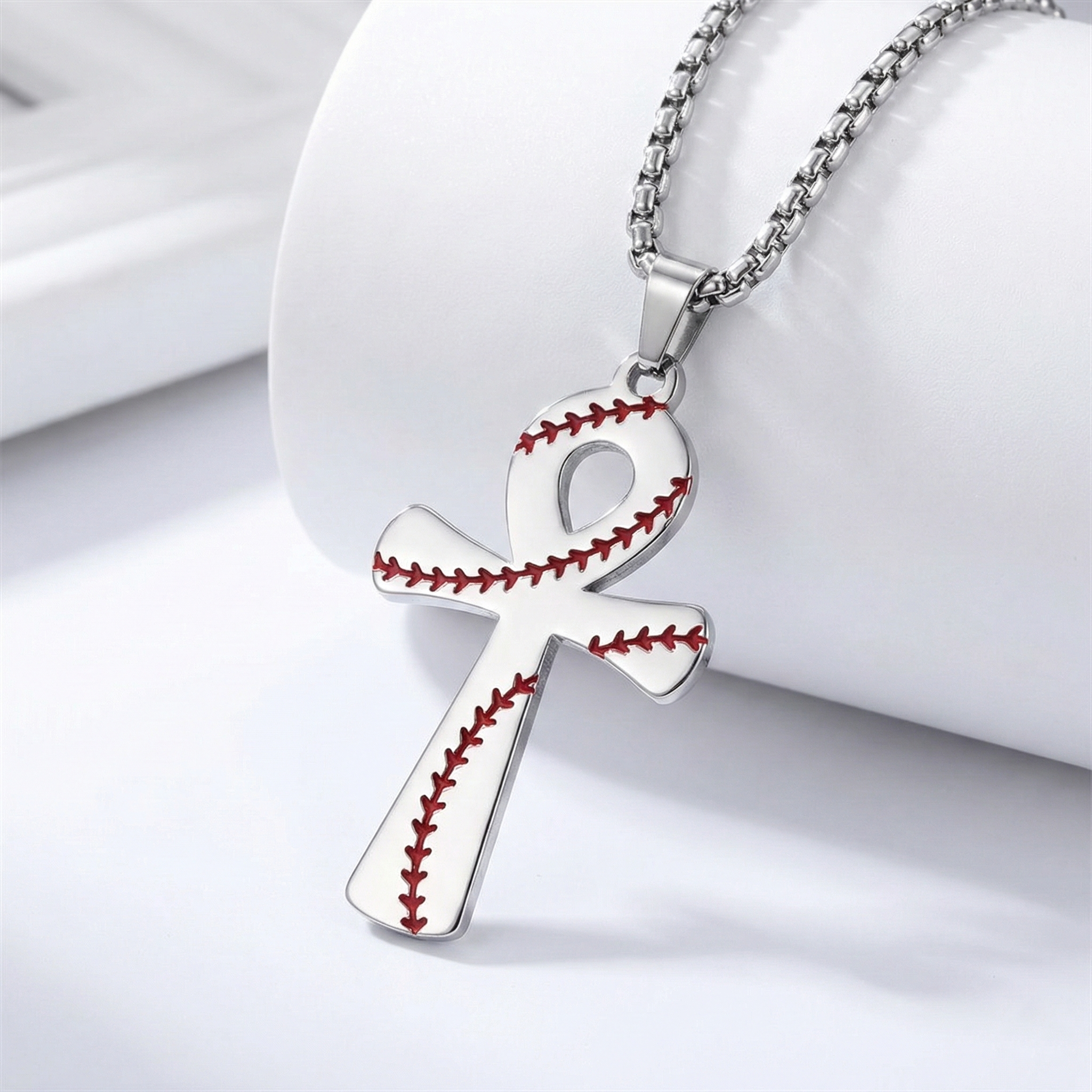 Silver cross-shaped pendant with baseball stitching design on a white background