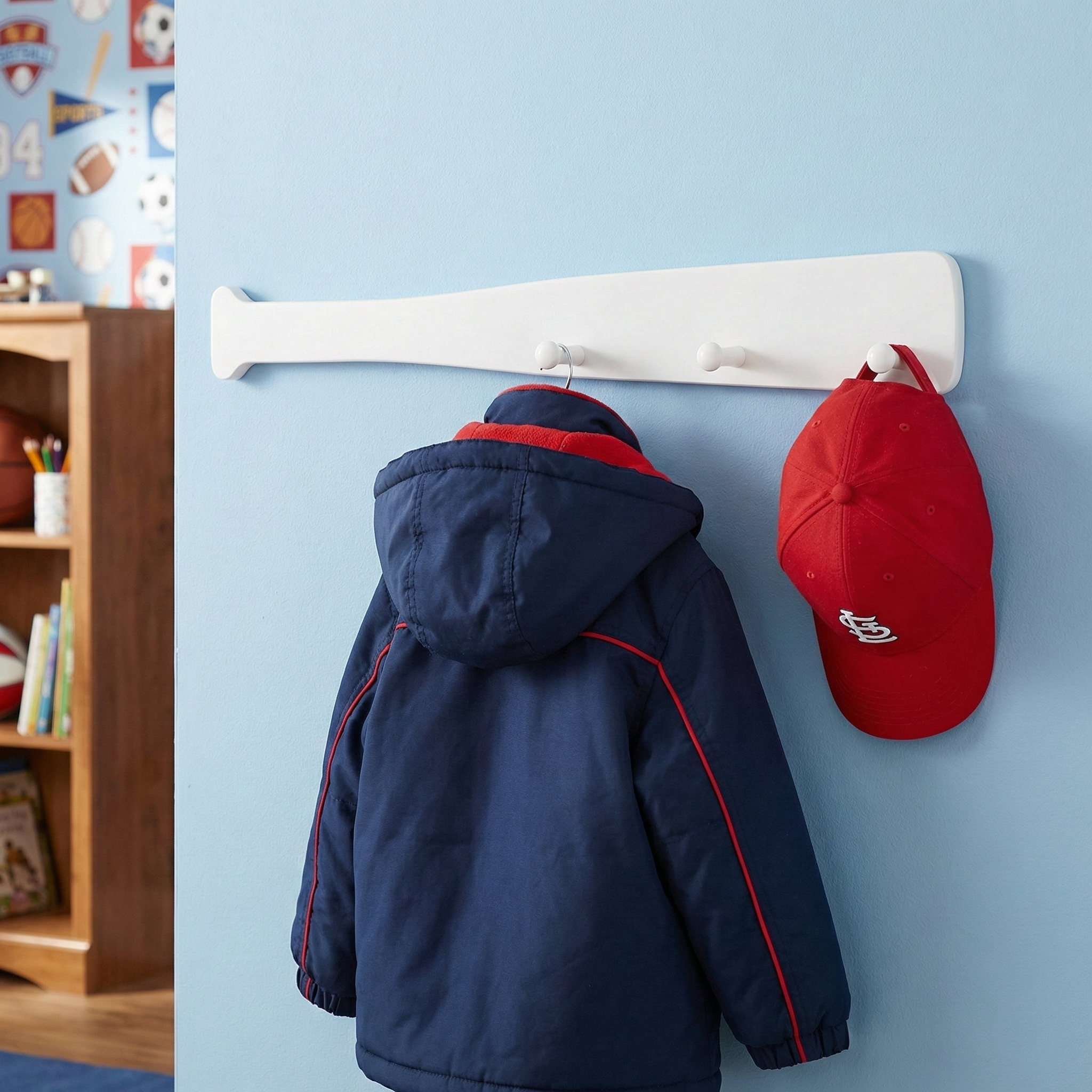 Navy jacket and red cap hanging on a white baseball bat coat rack against a blue wall.