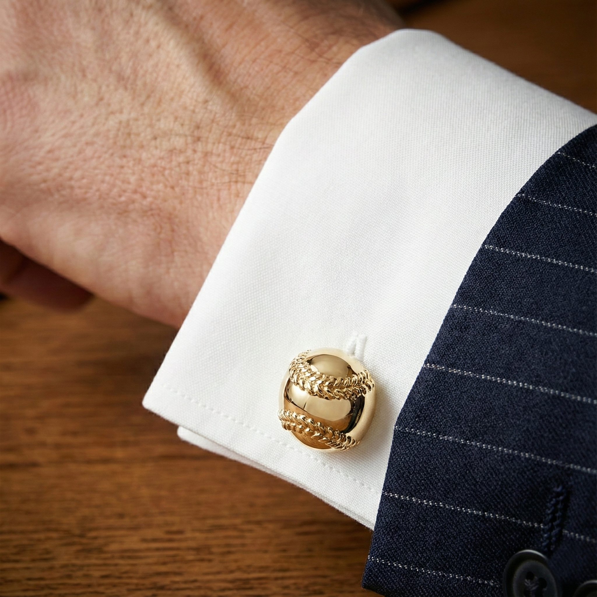 Gold baseball cufflink on a white cuff against a dark suit background