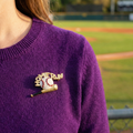 Purple sweater with a 'Home Run' baseball pin on a blurred ballpark background