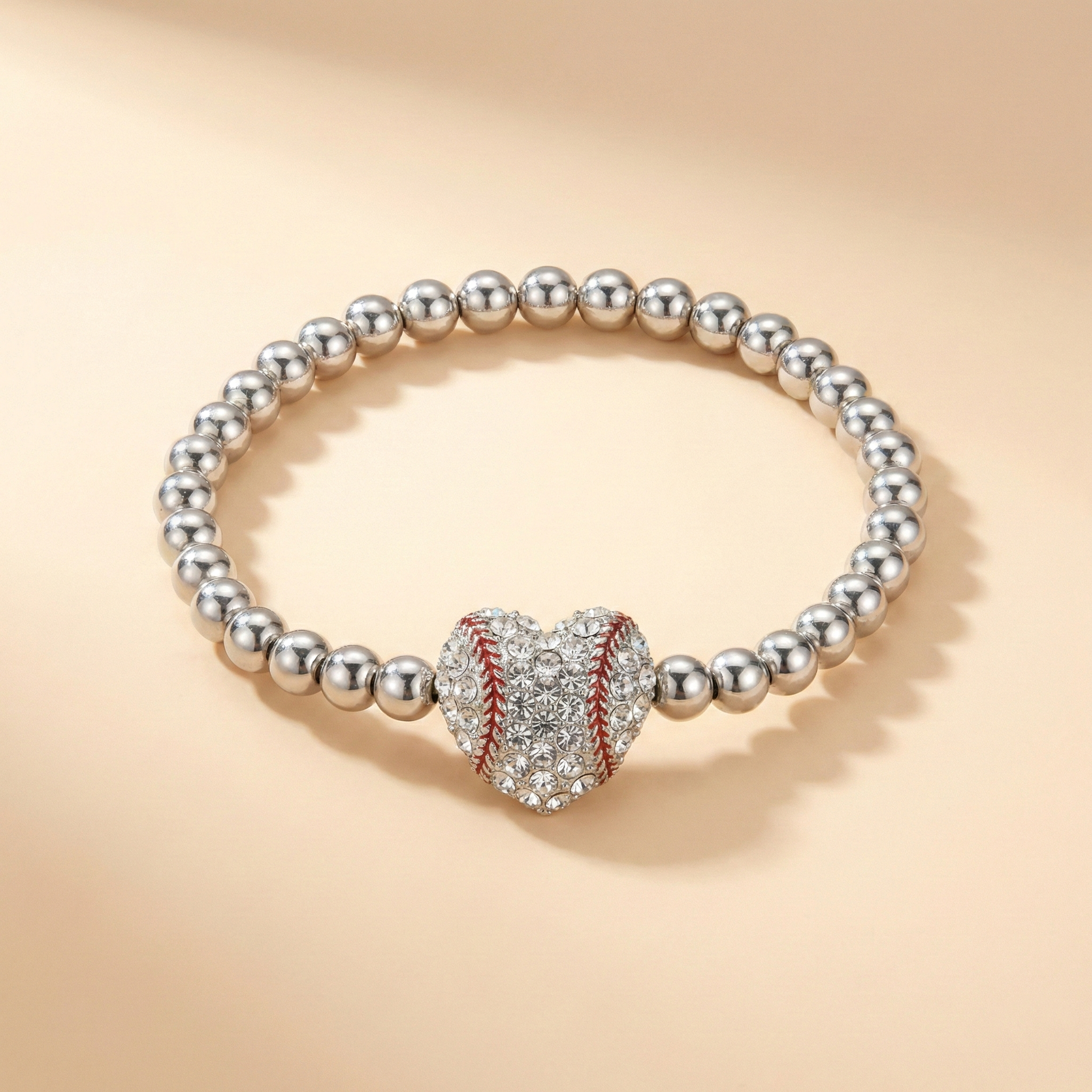 Silver bead stretchy bracelet with a crystal baseball heart-shaped charm on a beige background