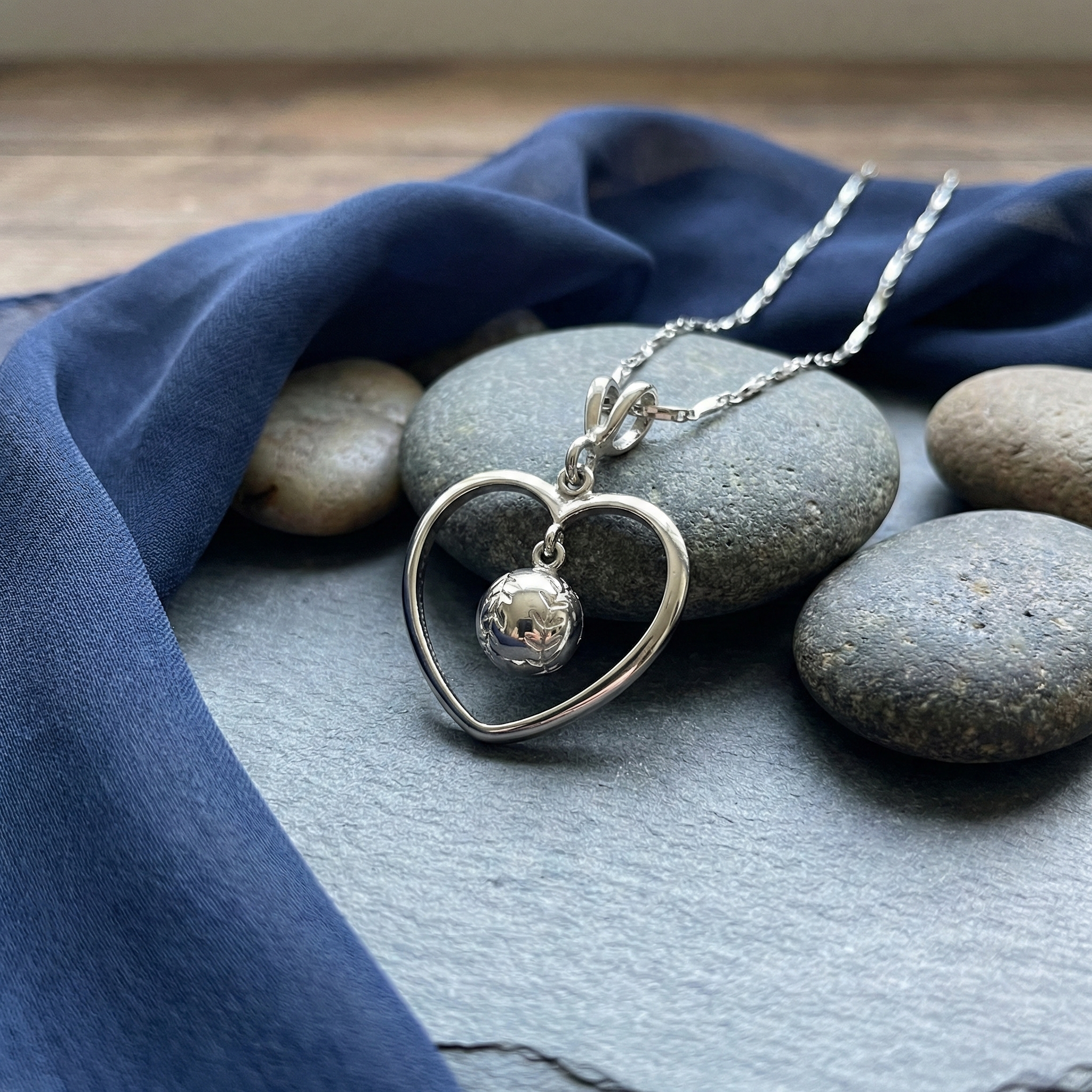 Sterling silver heart-shaped baseball necklace with a pendant on a stone surface with blue fabric