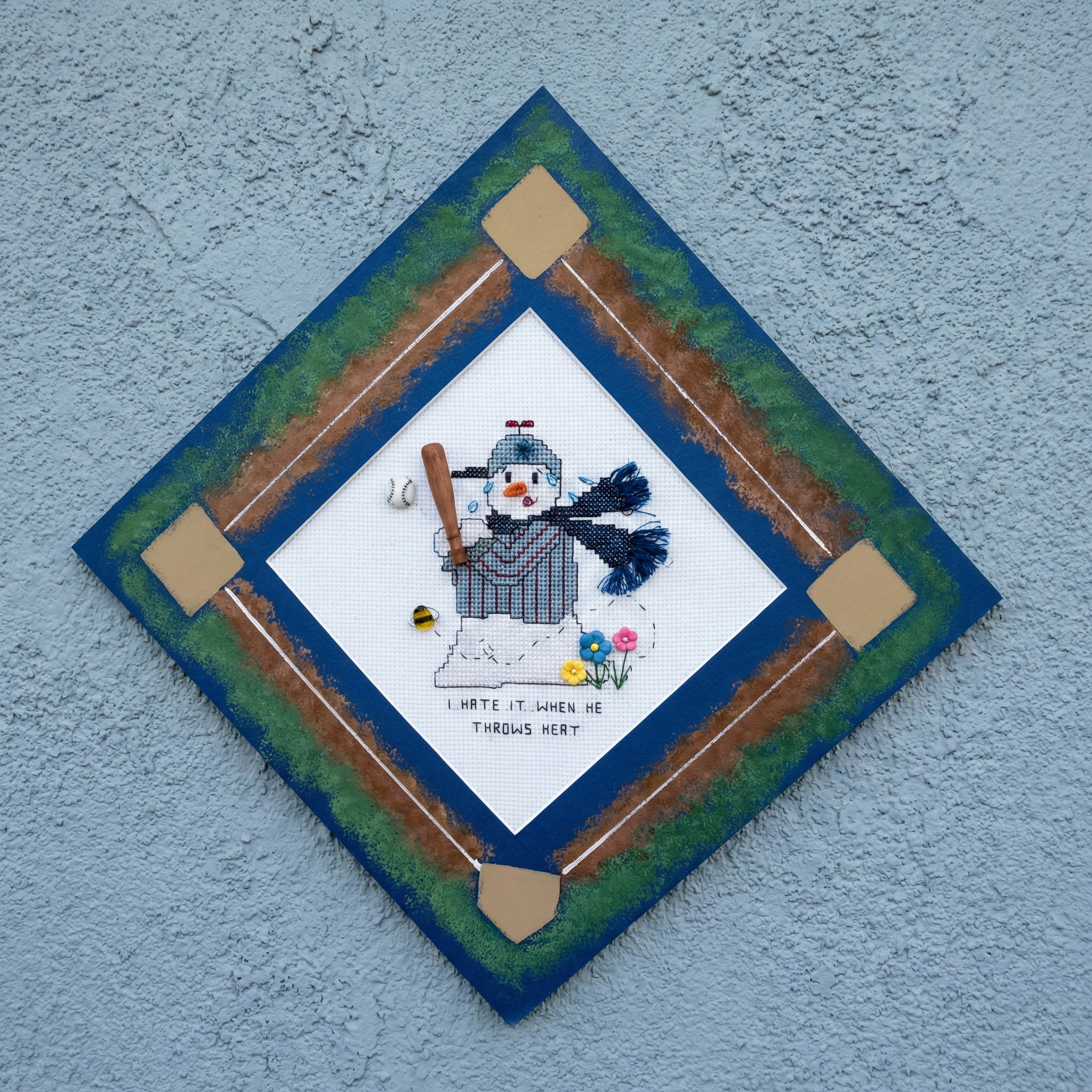 Cross-stitched baseball snowman needlepoint pattern with a broom on a diamond-shaped patch with a blue border.