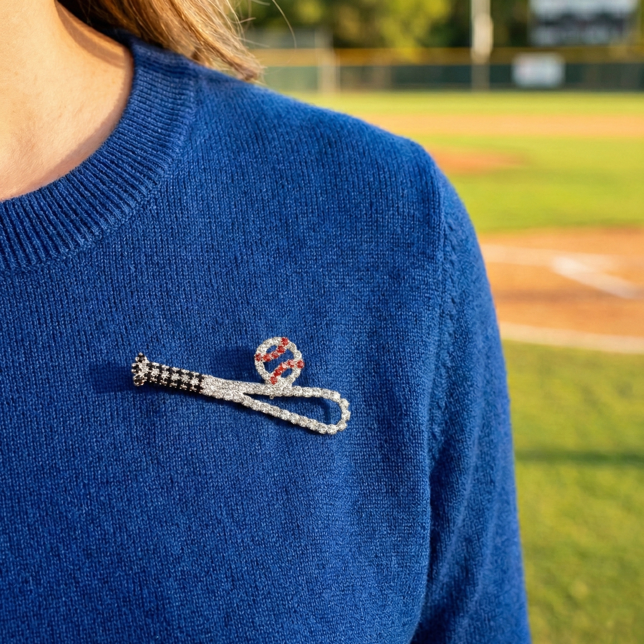 Blue sweater with a brooch pin featuring a baseball bat and ball on a baseball field background