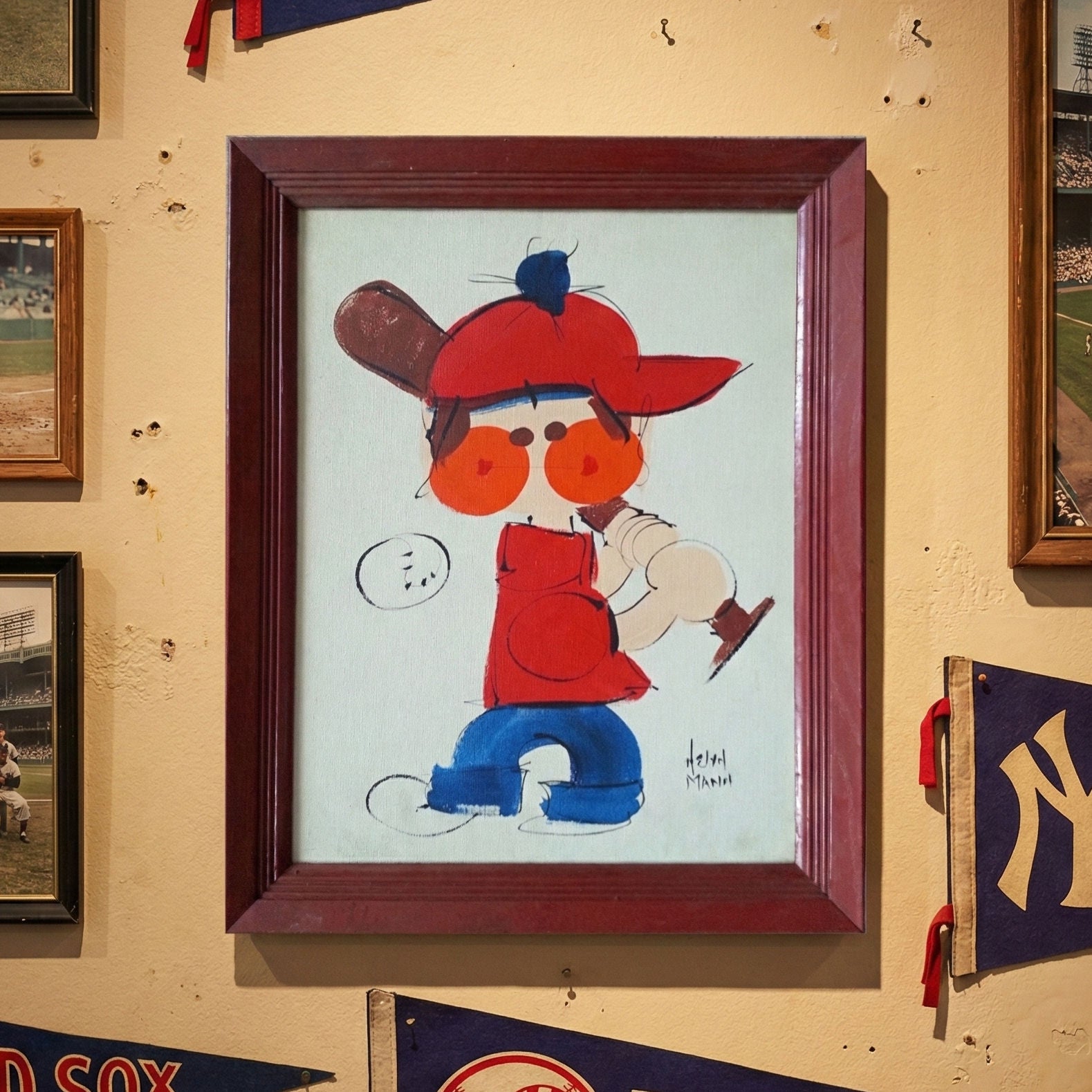 Helyn Mann original baseball canvas painting framed illustration of a child in a red cap and orange glasses on a wall with sports memorabilia.