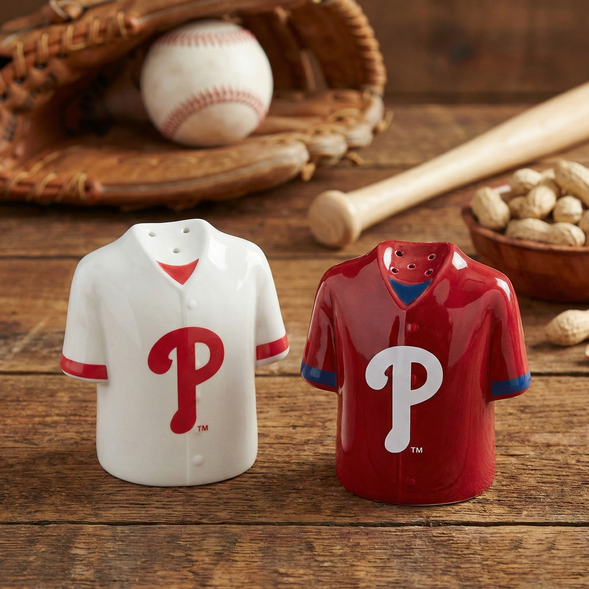 Two ceramic salt and pepper shakers in Phillies jersey designs on a wooden surface with baseball equipment.
