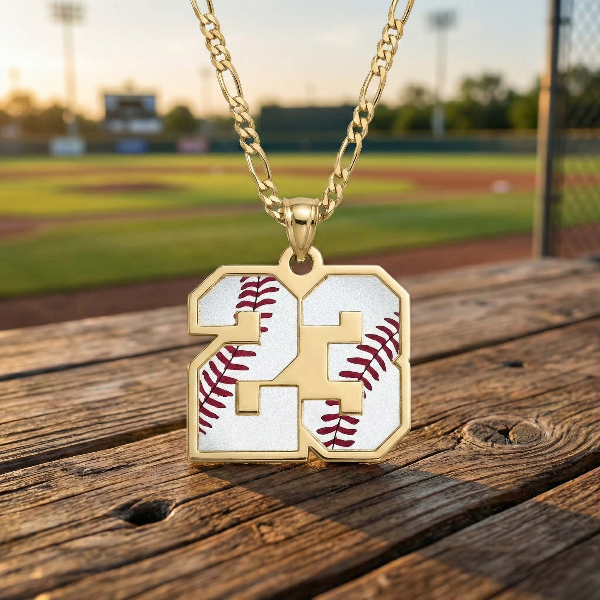 Gold necklace with a personalized pendant featuring the number 23 and baseball design on a wooden surface with a baseball field background.