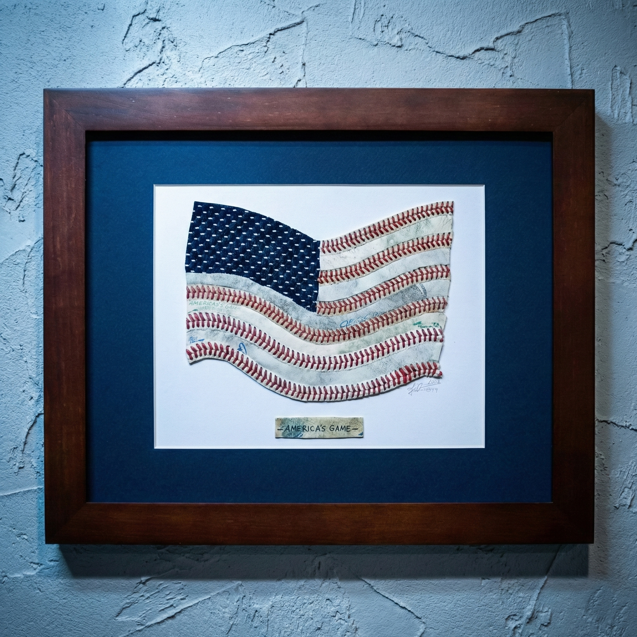 Framed artwork of an American flag made from baseballs on a textured blue wall.