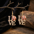 Gold 'LOVE' earrings with red and white baseball shaped charms on a wooden branch background