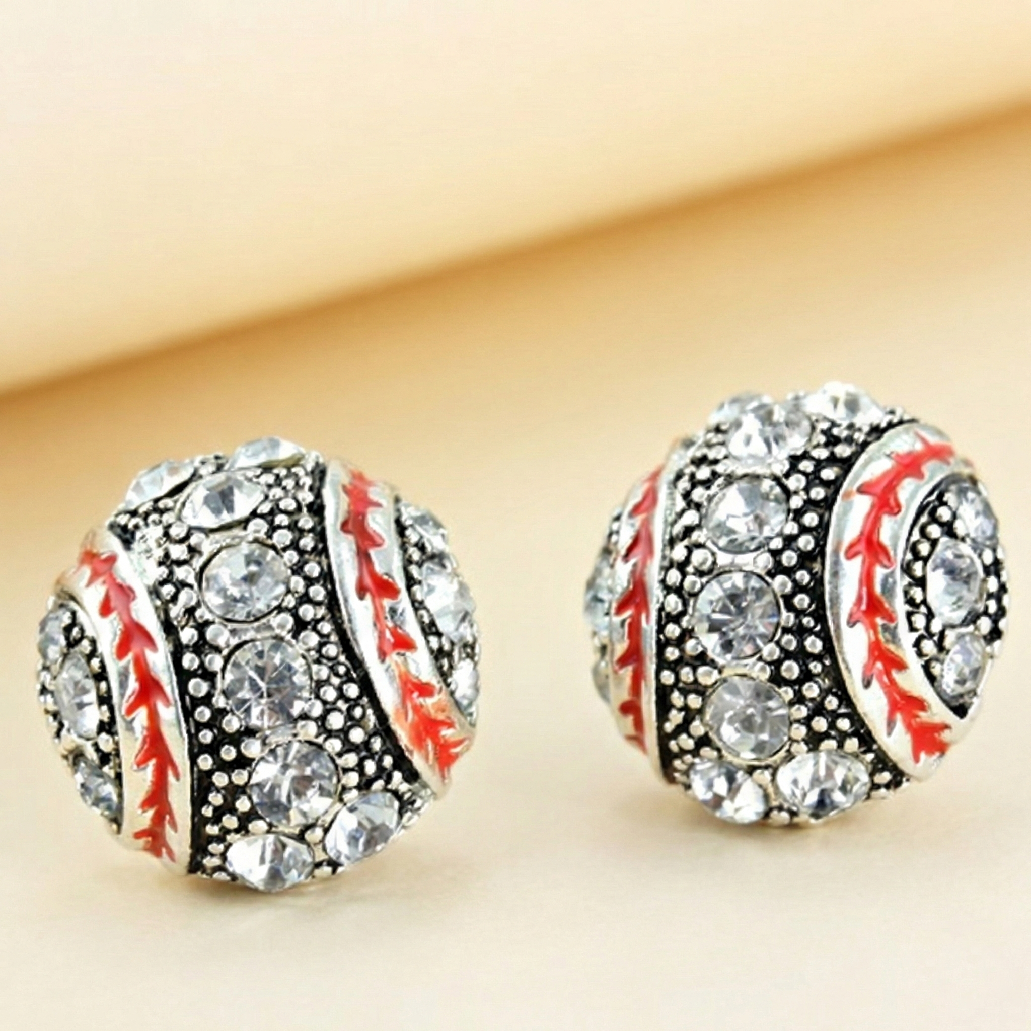 Baseball-shaped crystal bling earrings with rhinestones on a beige background