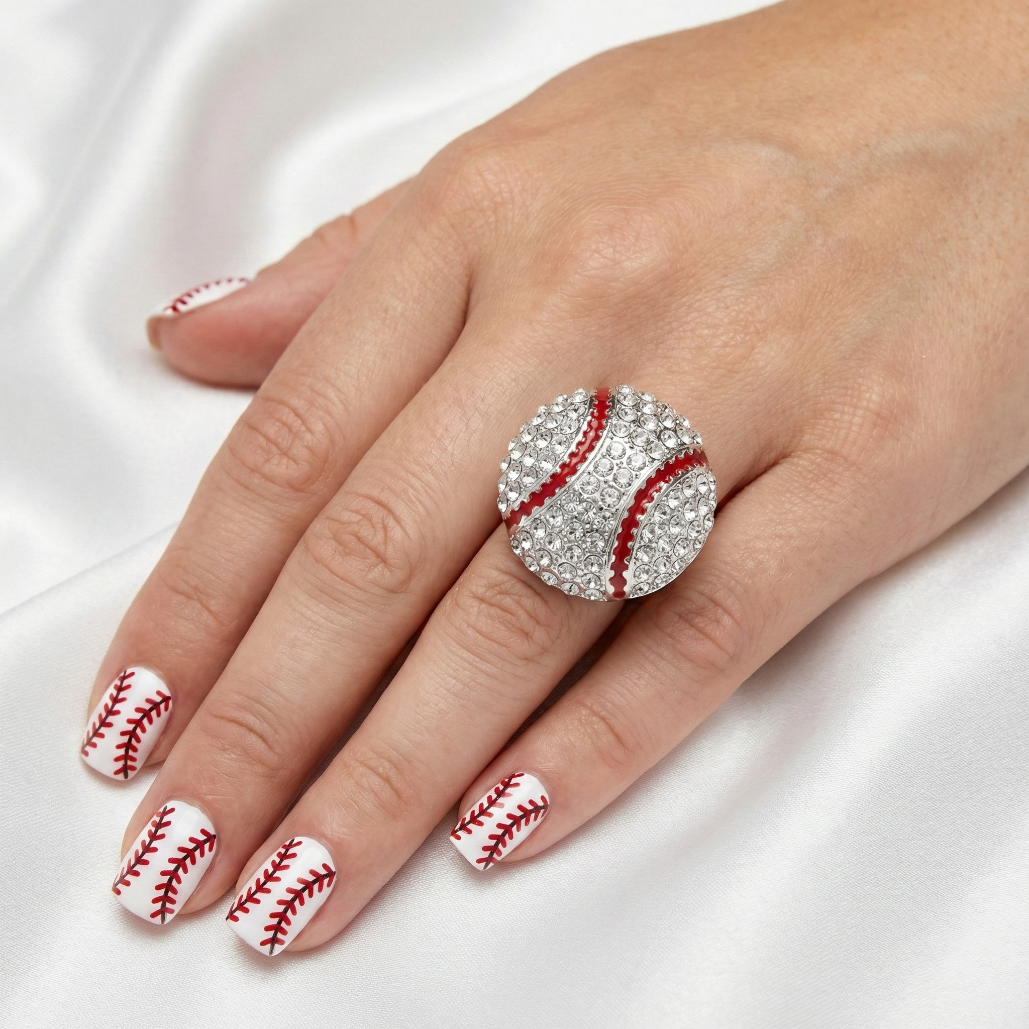 Hand wearing a baseball-themed ring with matching nail design on a white background