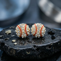Decorative earrings resembling baseballs with gemstones on a dark stone surface