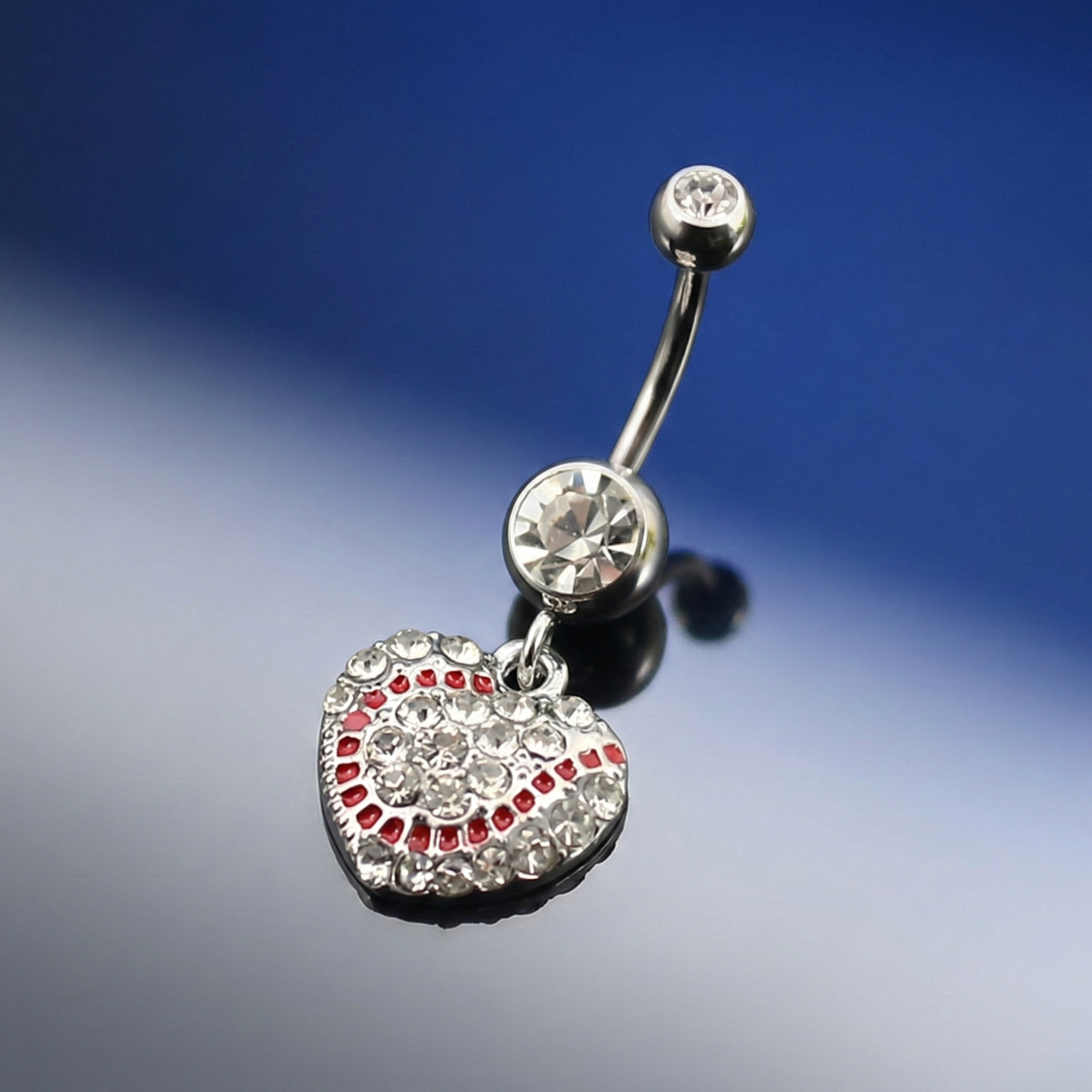 Belly button ring with heart-shaped baseball pendant and red stones on a gradient blue and gray background