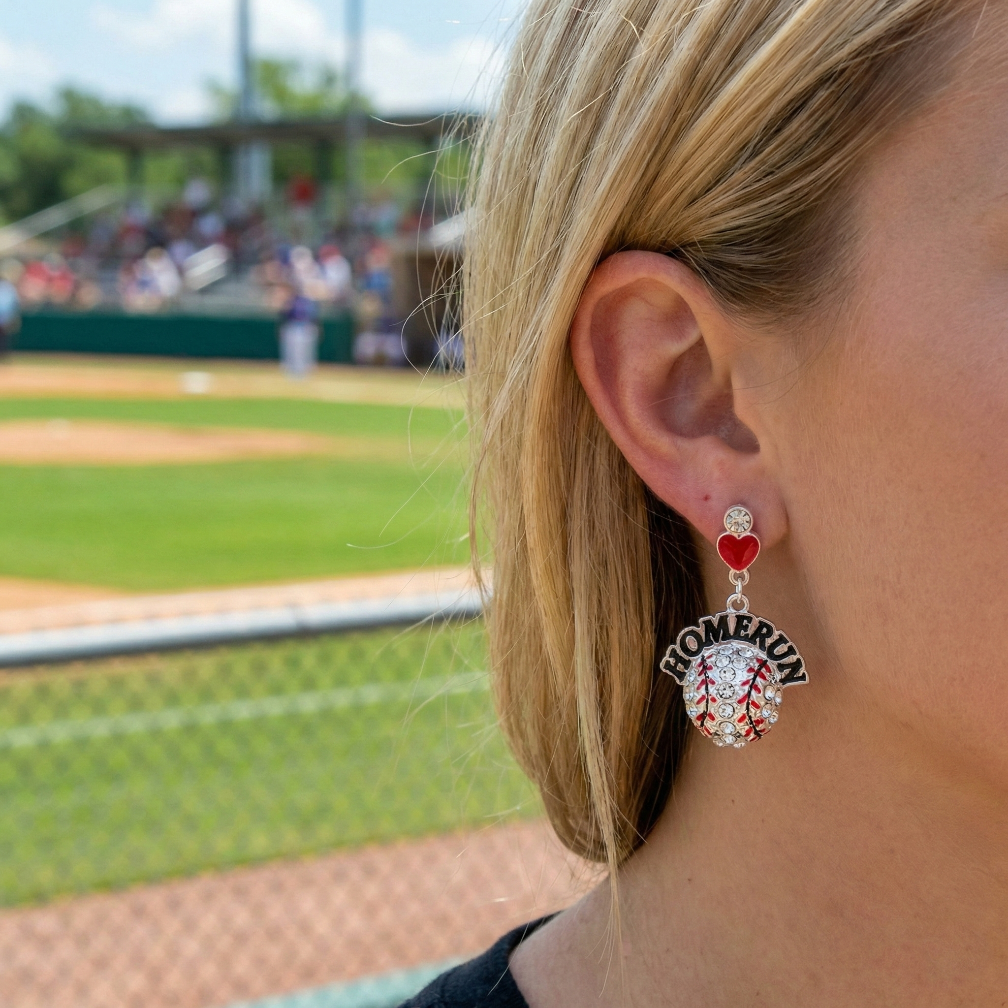 Person wearing a homerun crystal baseball-themed earring with a field in the background