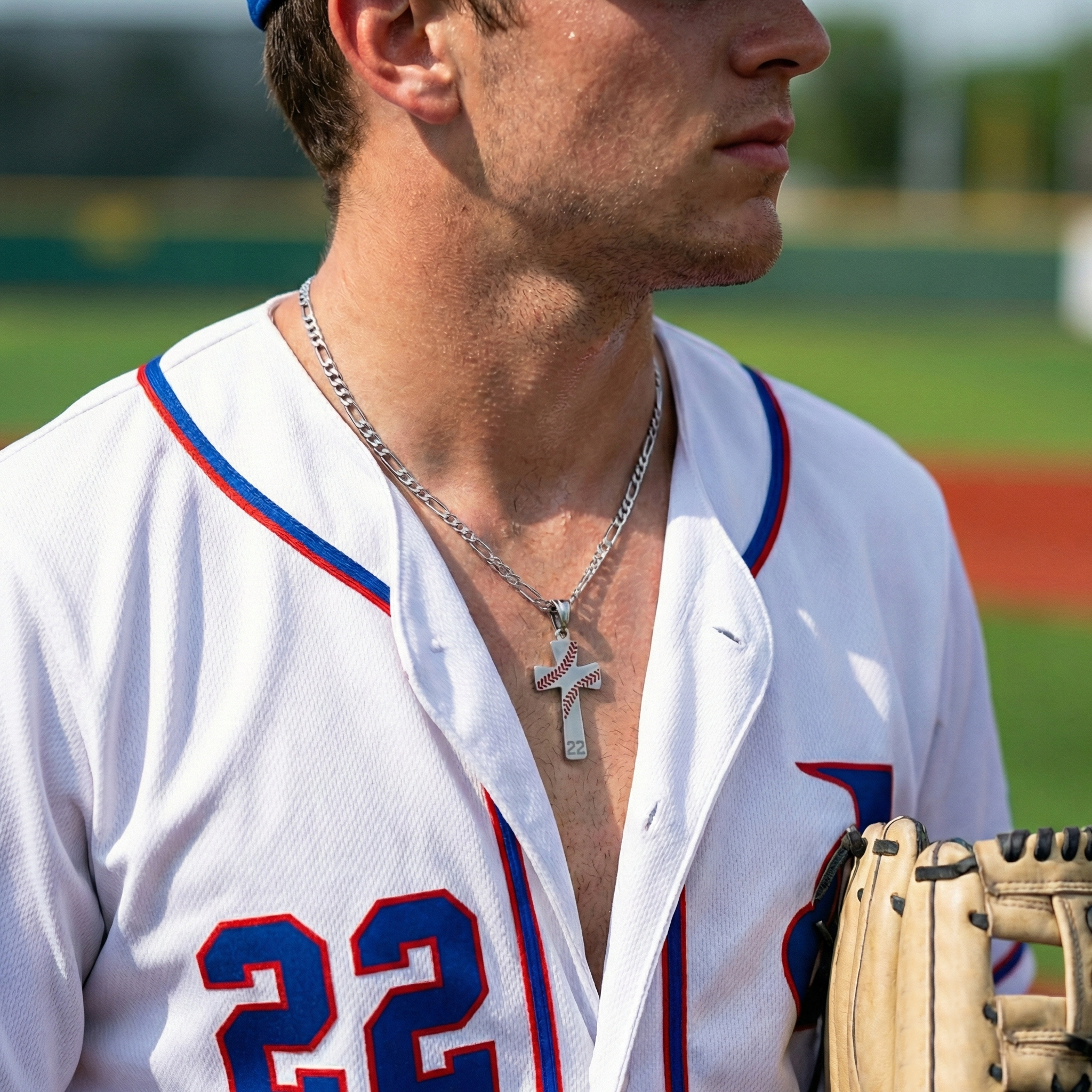 Baseball player wearing a white jersey with red and blue accents and a silver baseball number cross necklace, holding a glove on a field.
