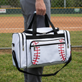 Person holding a white duffel bag with baseball stitching design on a grassy field.