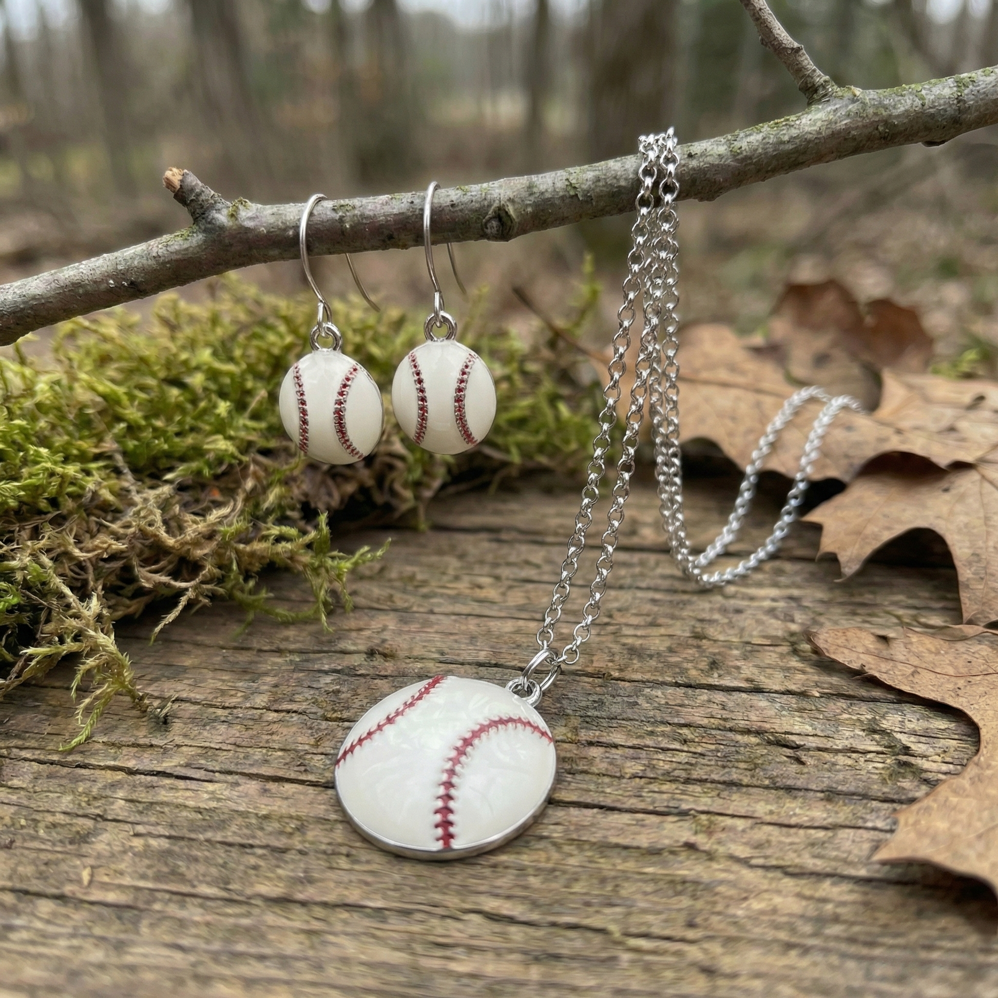 Baseball-themed jewelry including a necklace and earrings on a natural background with leaves and moss.