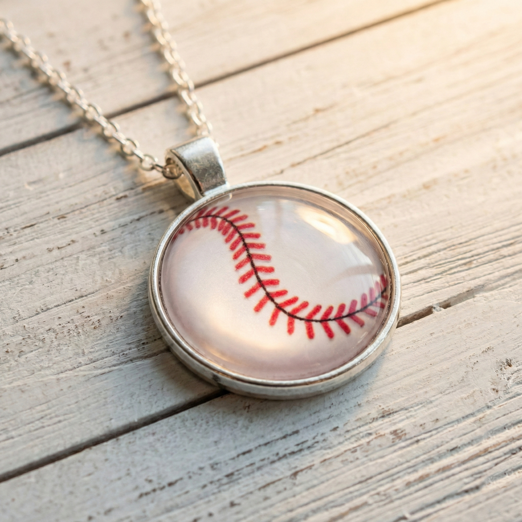 Silver necklace with a pendant shaped like a baseball on a wooden surface