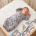 Newborn baby in a gown sleeping in a crib with a baseball-themed blanket