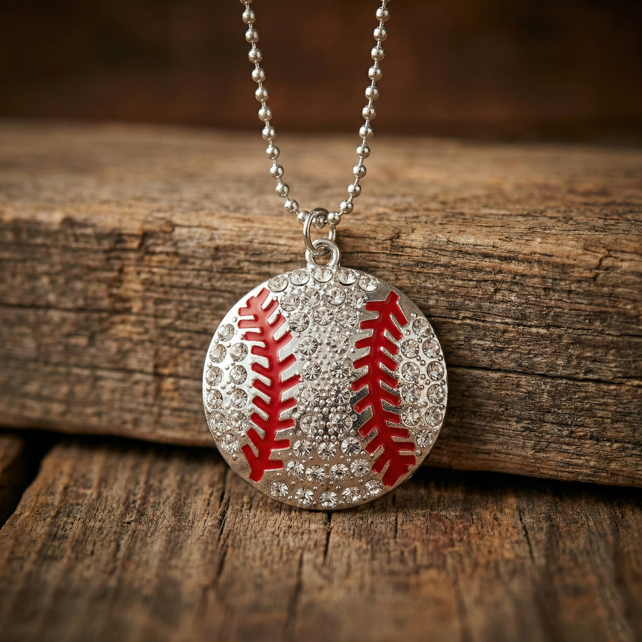 Baseball-shaped pendant with red stitching on a silver chain, placed on wooden surface