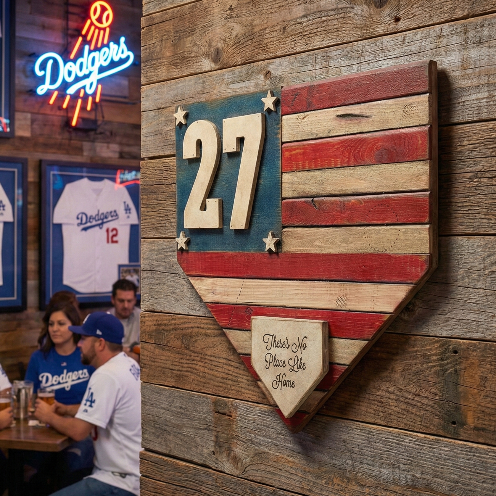 Wooden baseball American Flag home plate decoration sign with number 27 on a wooden wall, with people sitting at a table in the background.