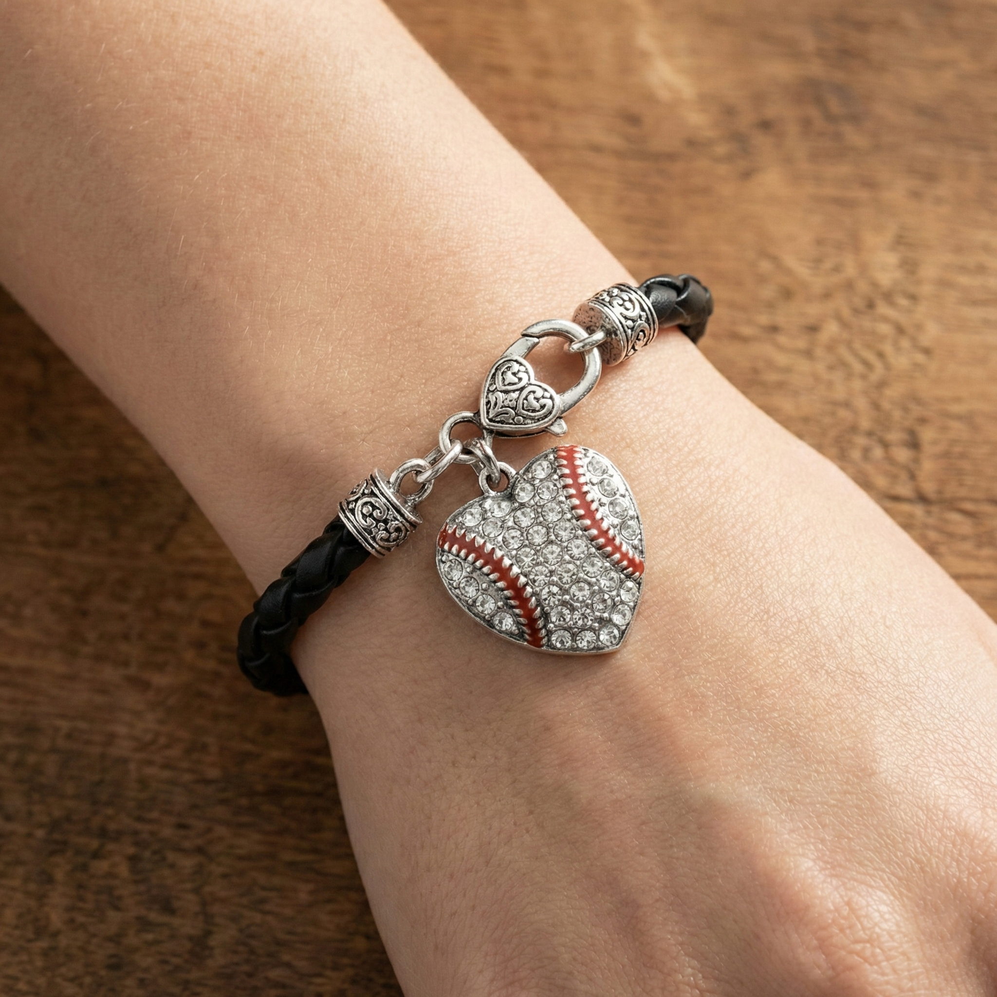 Black leather bracelet with heart-shaped baseball charm on a wrist against a wooden background