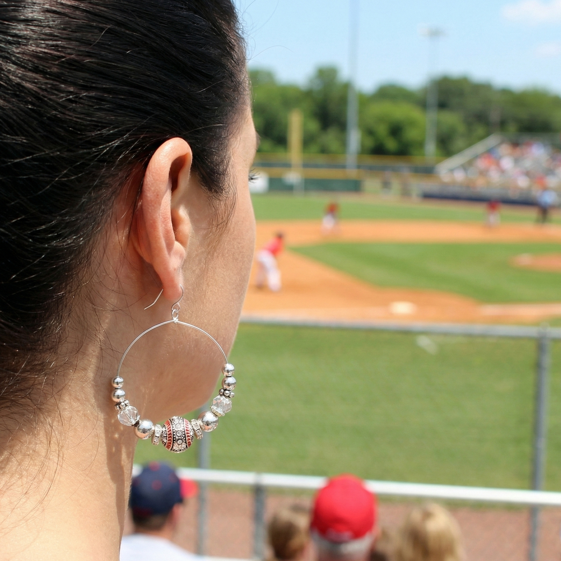Person watching a baseball game from behind, with a focus on their baseball earring.