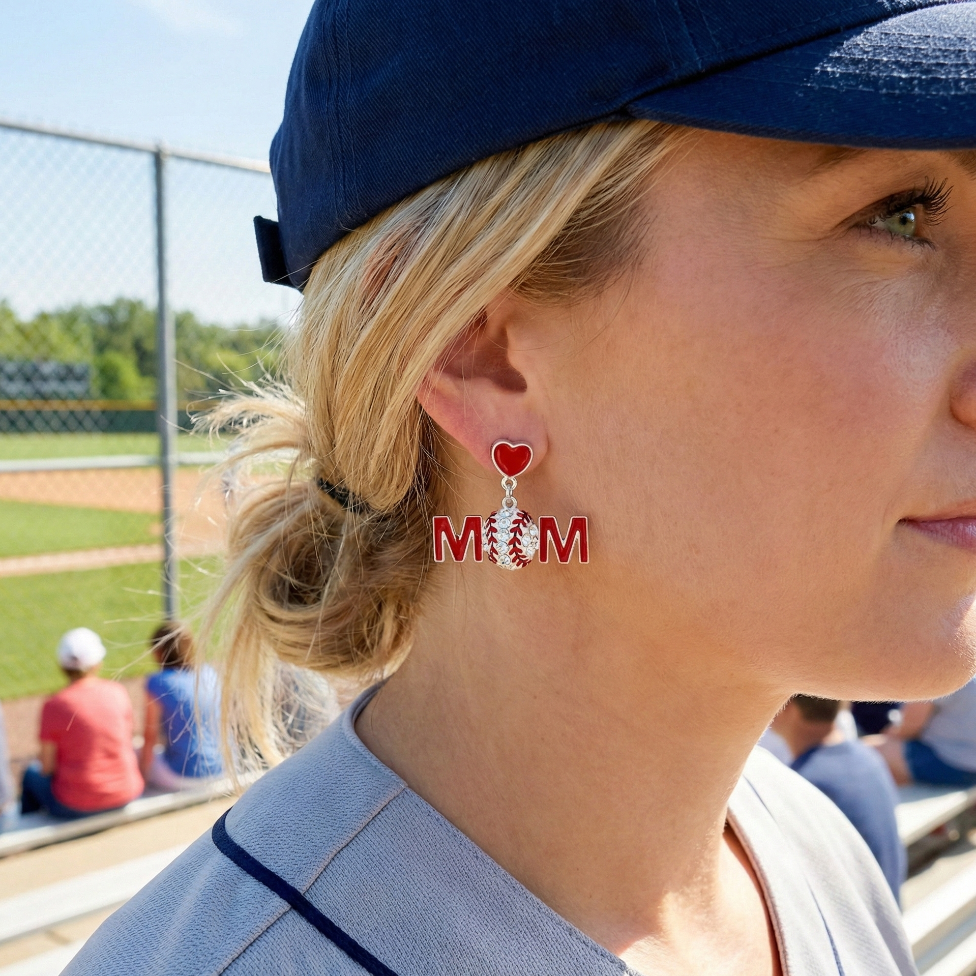 Woman wearing earrings with baseball mom and a red heart design at a sports event.