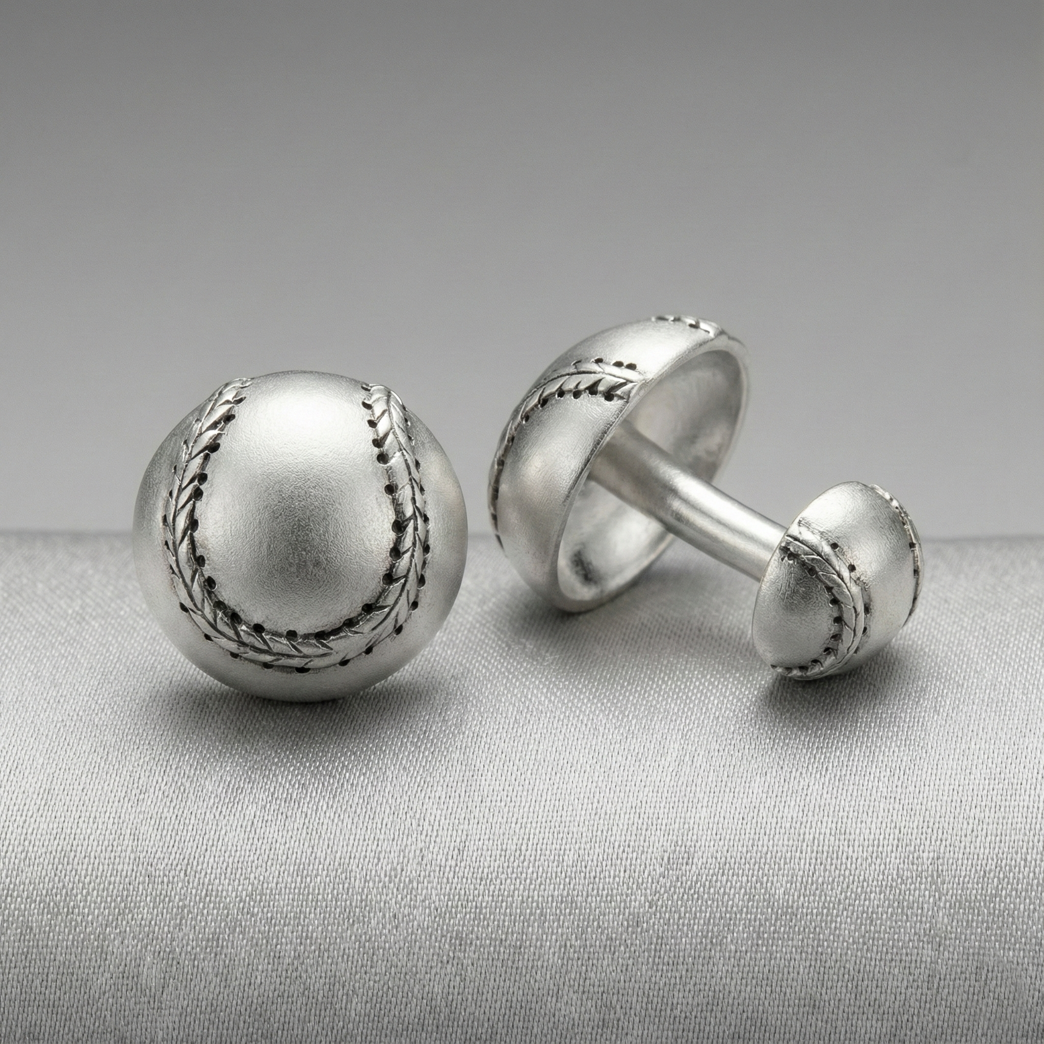 Silver baseball cufflinks on a gray fabric background
