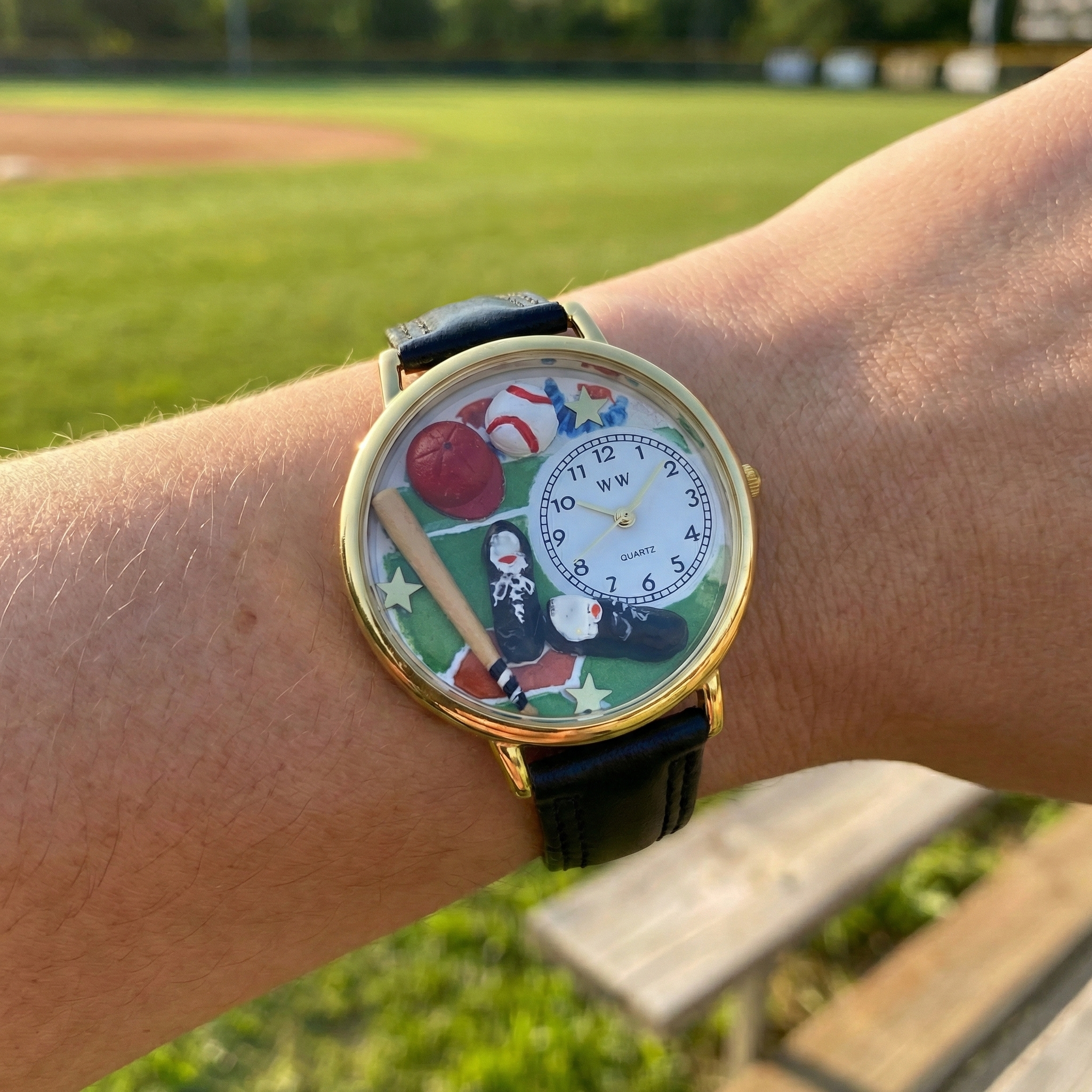 Wrist wearing a watch with a colorful baseball themed face on a grassy field background