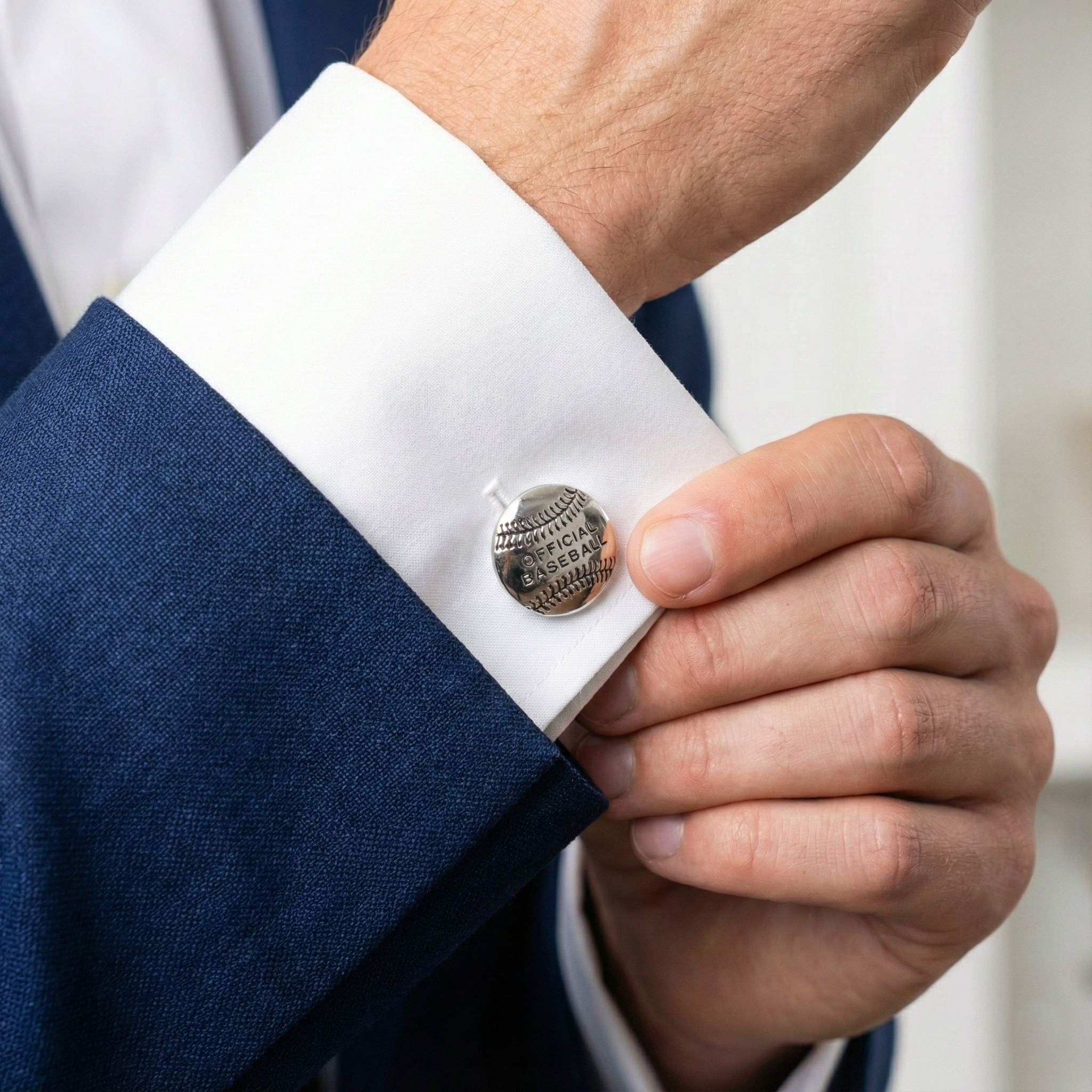 Close-up of a person adjusting a baseball cufflink on a blue suit sleeve.