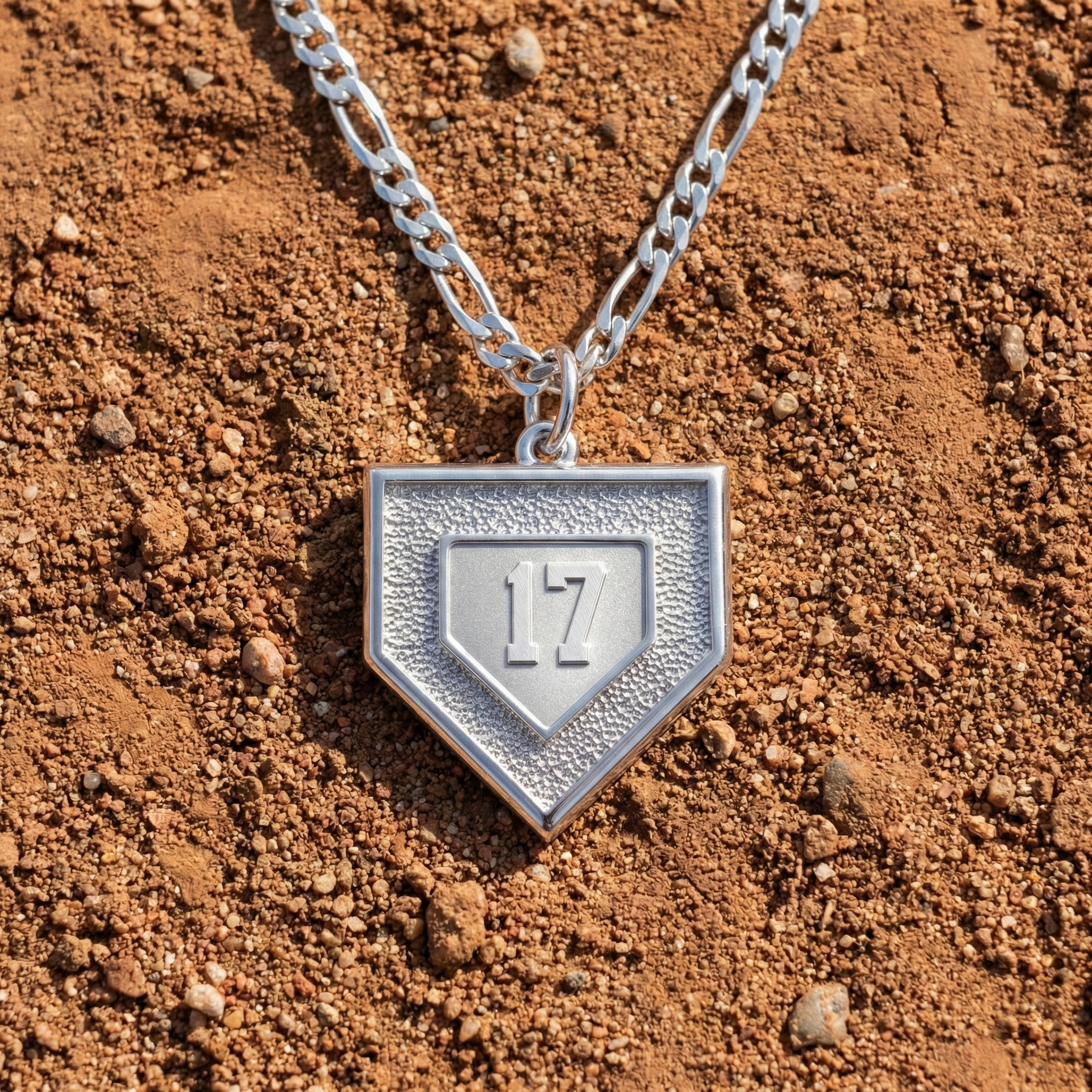 Silver necklace with a baseball pendant shaped like a home plate on a dirt surface