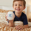 Child holding a tooth fairy baseball pillow, sitting on a bed.