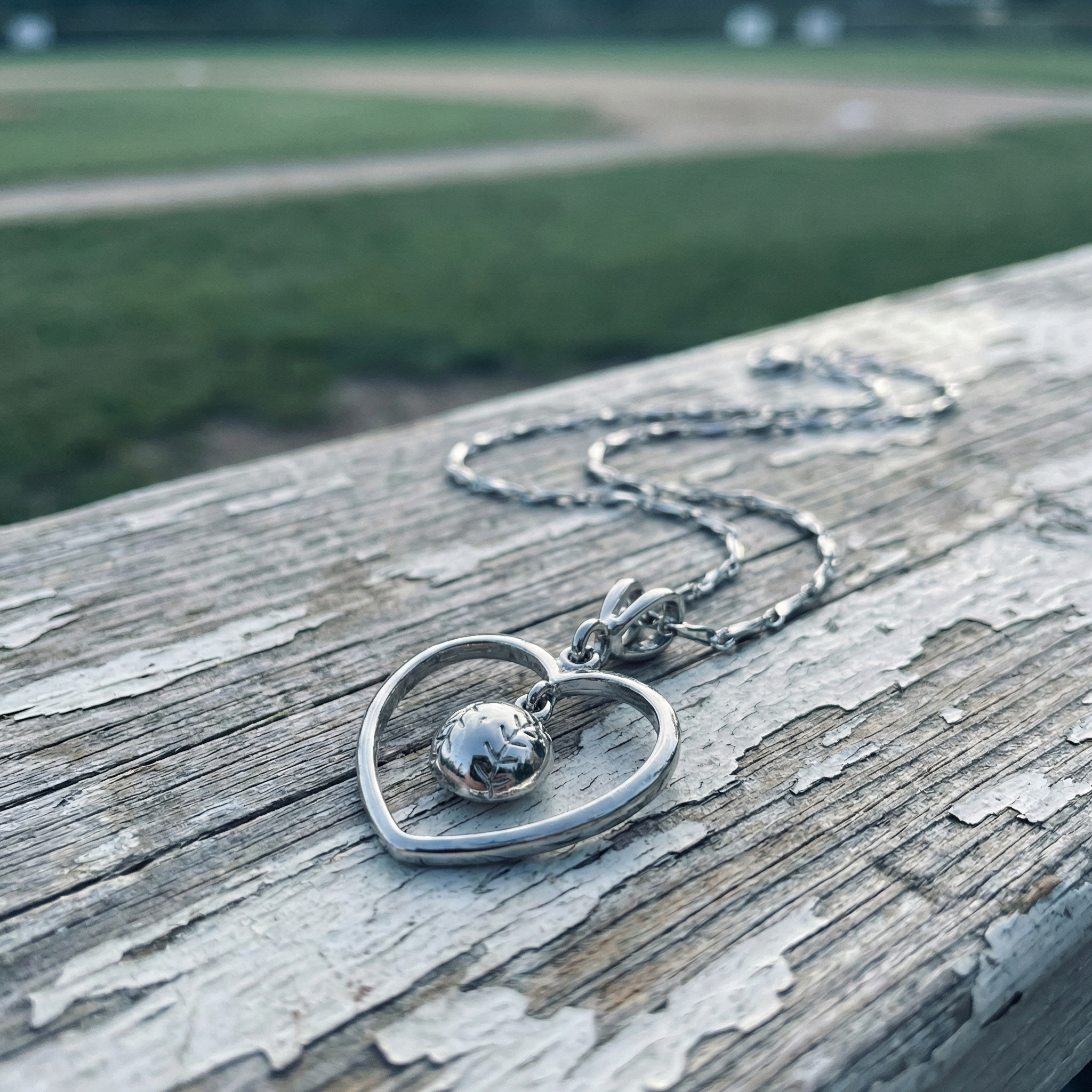 Sterling silver heart-shaped baseball necklace with a small round baseball pendant on a wooden surface with a blurred natural background