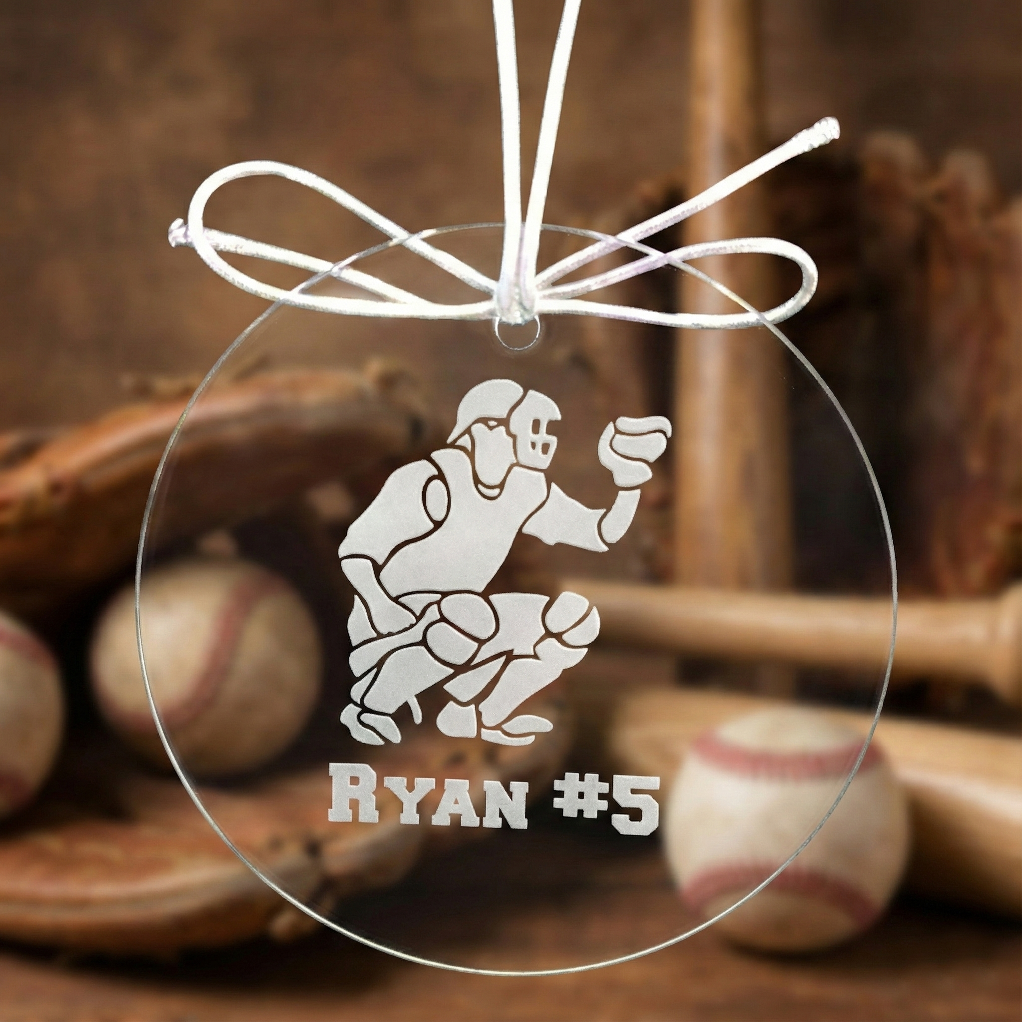 Clear glass baseball catcher ornament including baseball player design, hanging against a baseball-themed background.