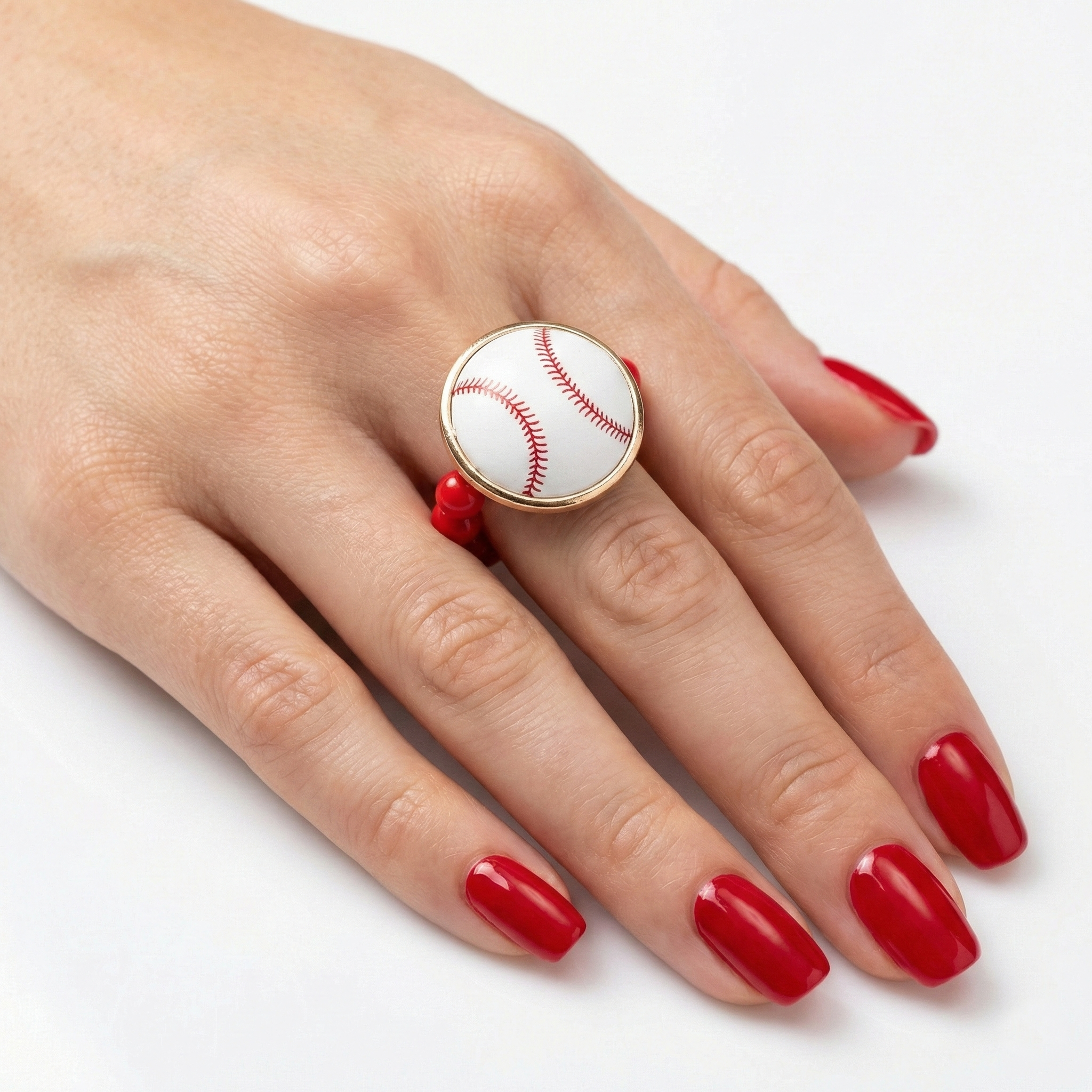Ring with a baseball design on a hand with red nail polish against a white background