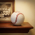 Baseball-shaped candle on a wooden shelf with a vintage baseball team photo in the background.