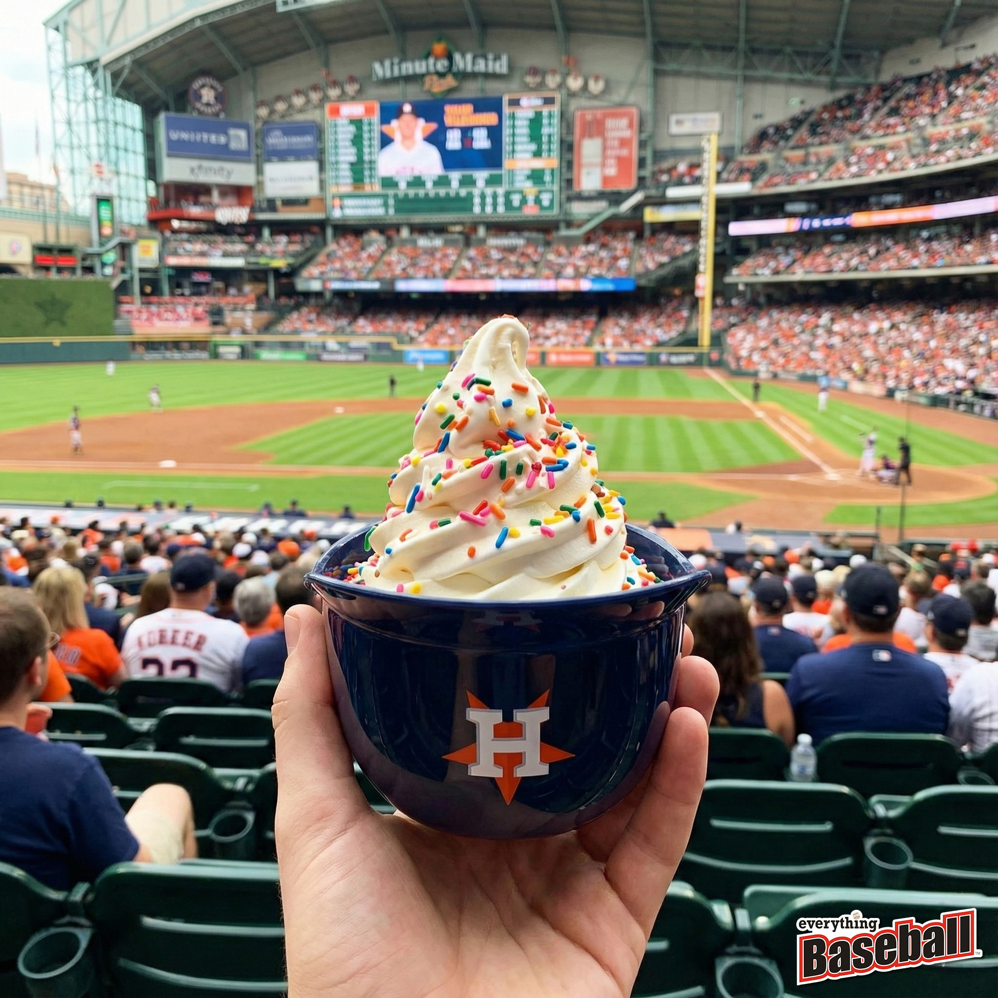 Hand holding a blue Houston Astros helmet bowl of ice cream with sprinkles at a baseball game.