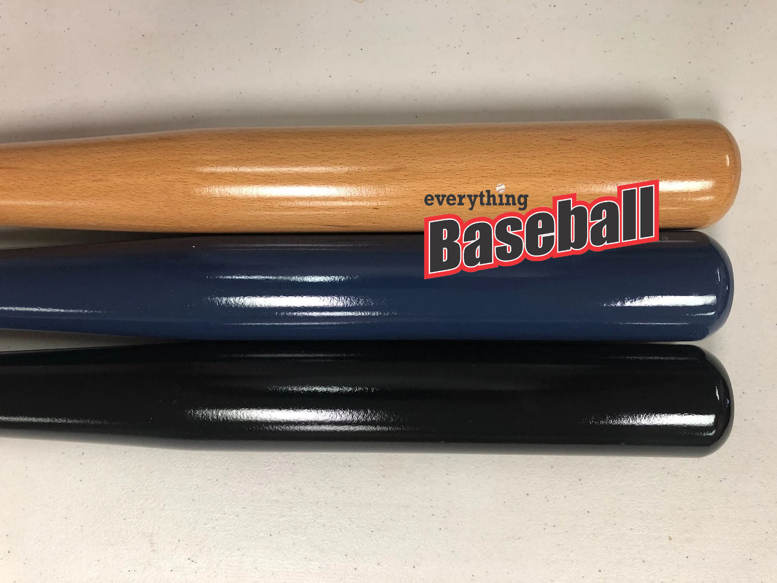 Three baseball bats of different colors (wooden, blue, black) with 'everythingBaseball' logo on a light background.