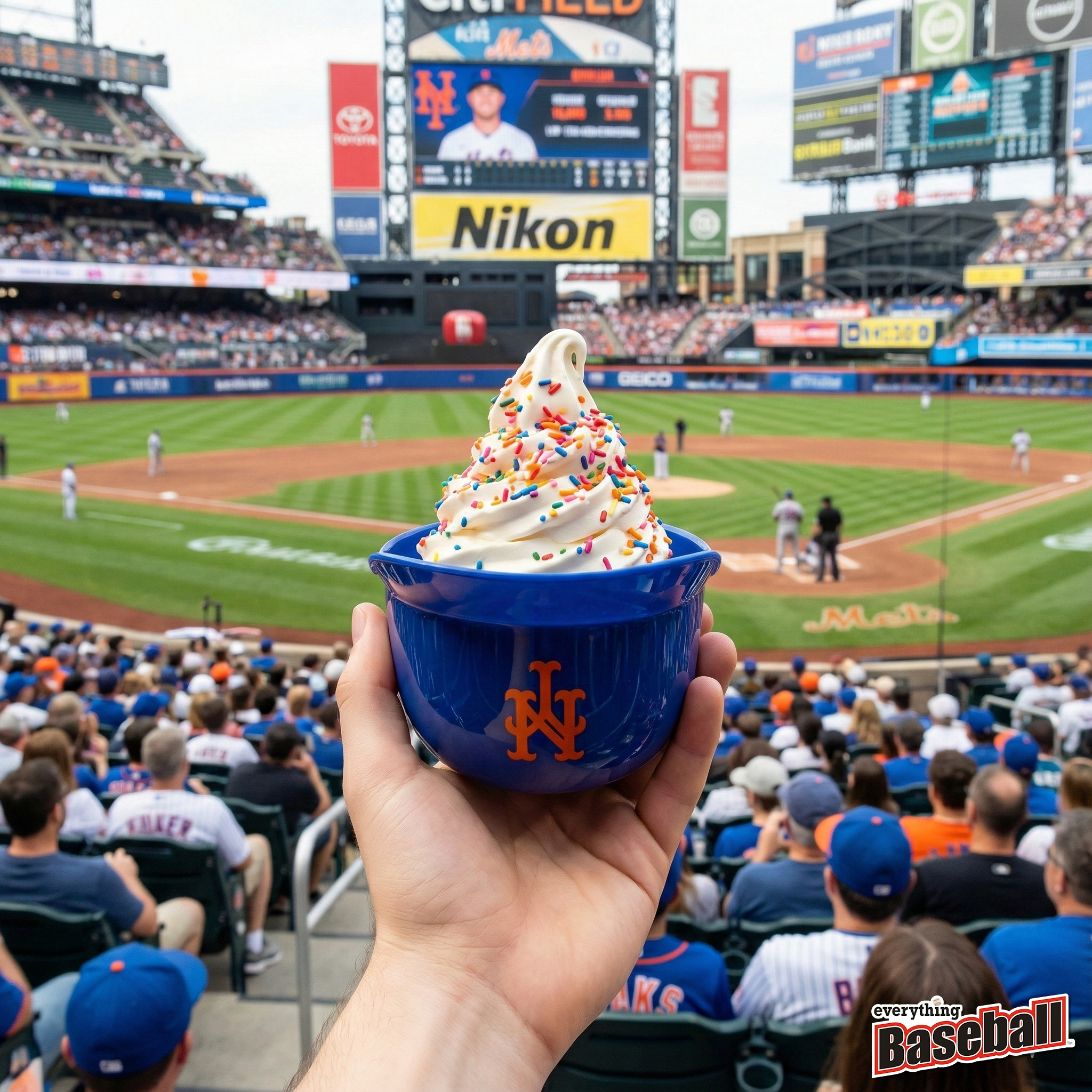 Blue New York Mets helmet cup with ice cream at a baseball game, held by a person.