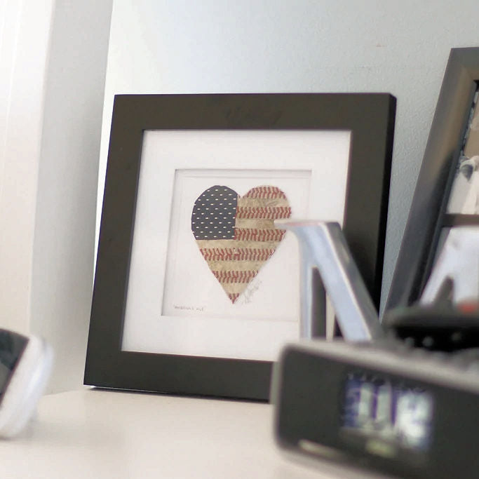 Framed baseball seams artwork of a heart with American flag design on a shelf.