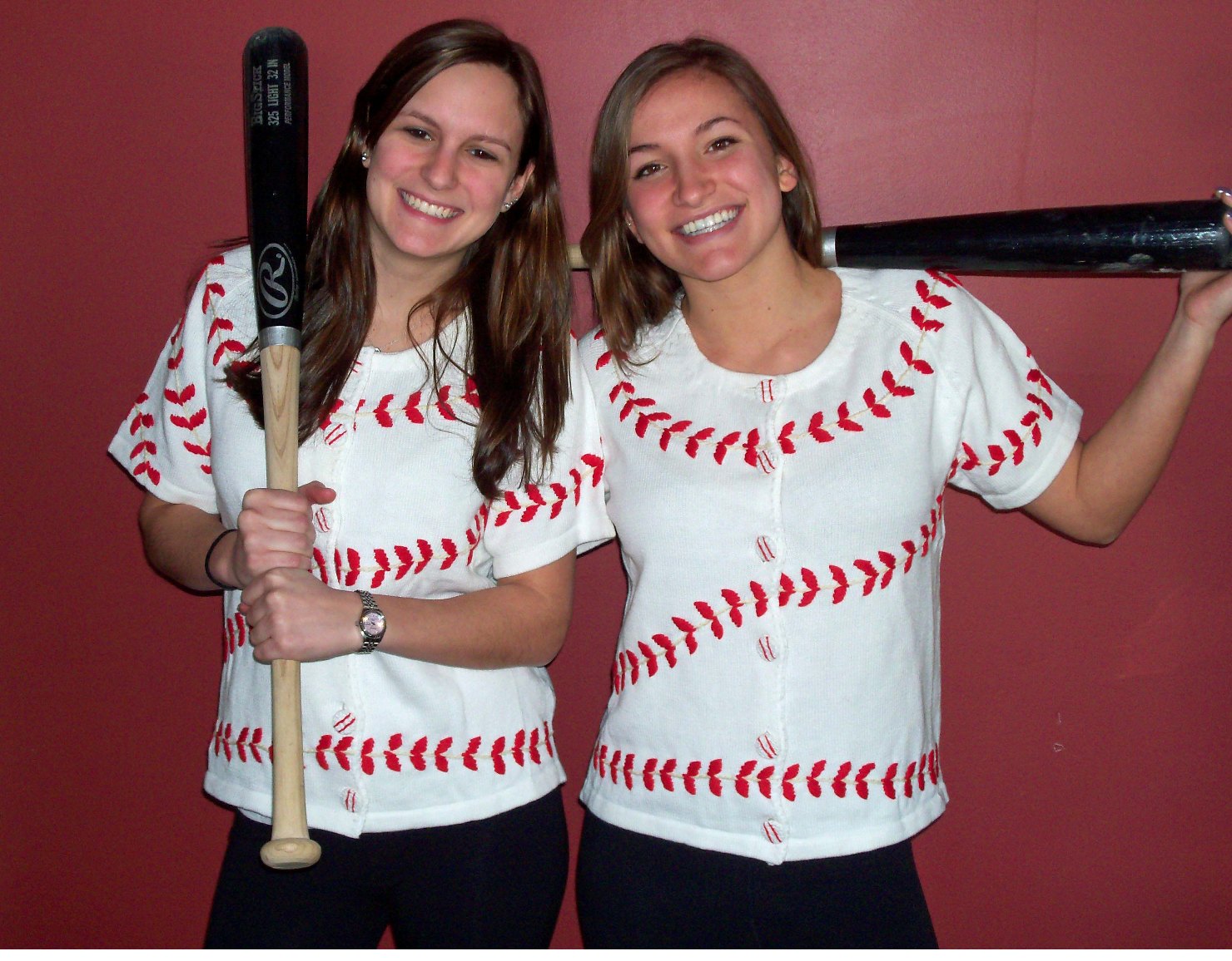 Two women wearing white baseball shirts with red stitching design, holding baseball bats against a red background.
